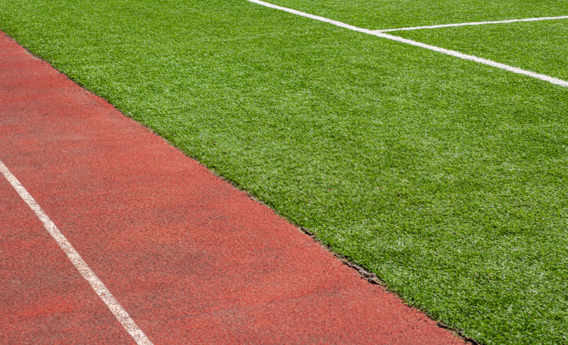 Athletics track alongside an artificial grass sports field in daylight