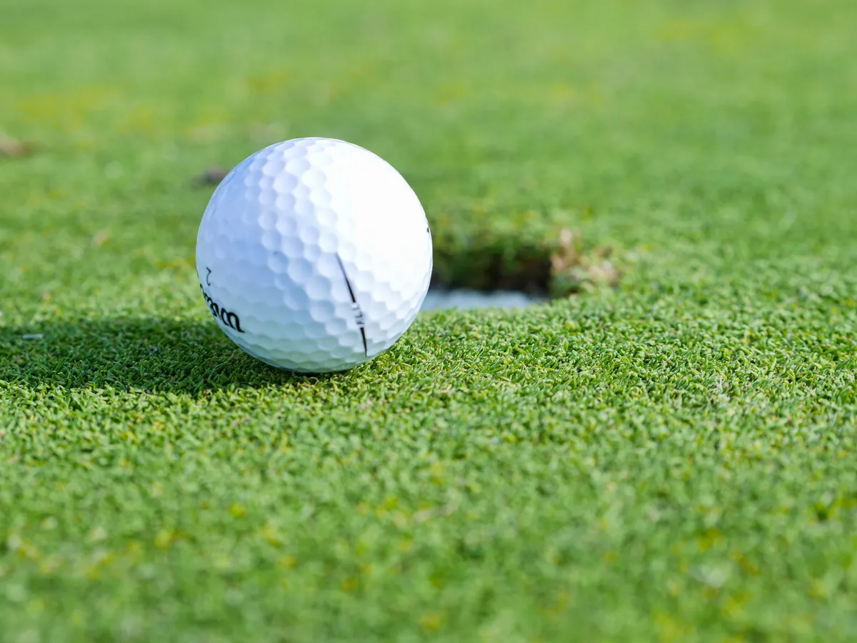 A golf ball resting beside the hole on a closely mown green