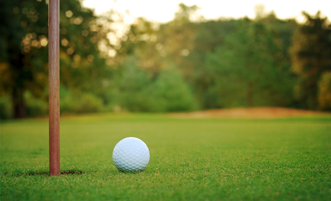 Golf ball resting beside the pin flag on a low-maintenance artificial putting green