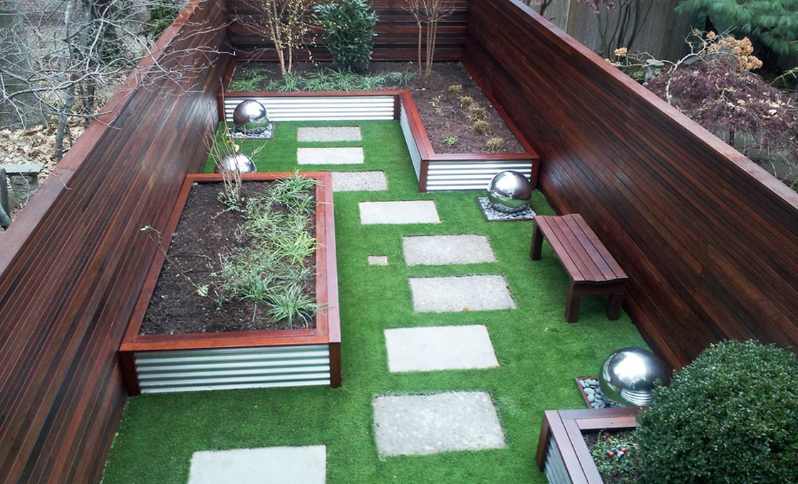 Contemporary urban courtyard garden utilizing horizontal cedar fencing, corrugated metal raised garden planters, stone pavers, and lush artificial grass