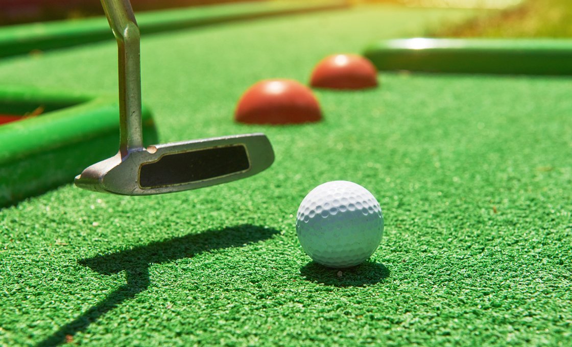 Putter addressing a golf ball on artificial putting turf