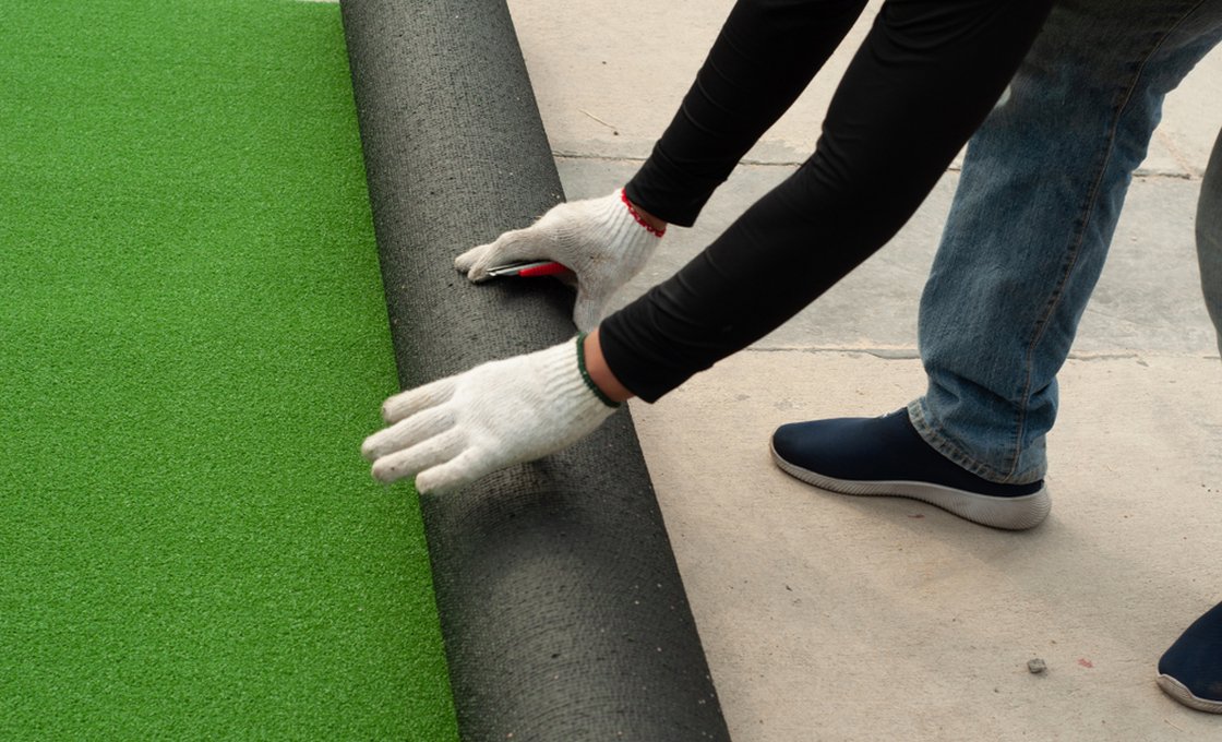 Installer unrolling artificial grass roll showing perforated backing