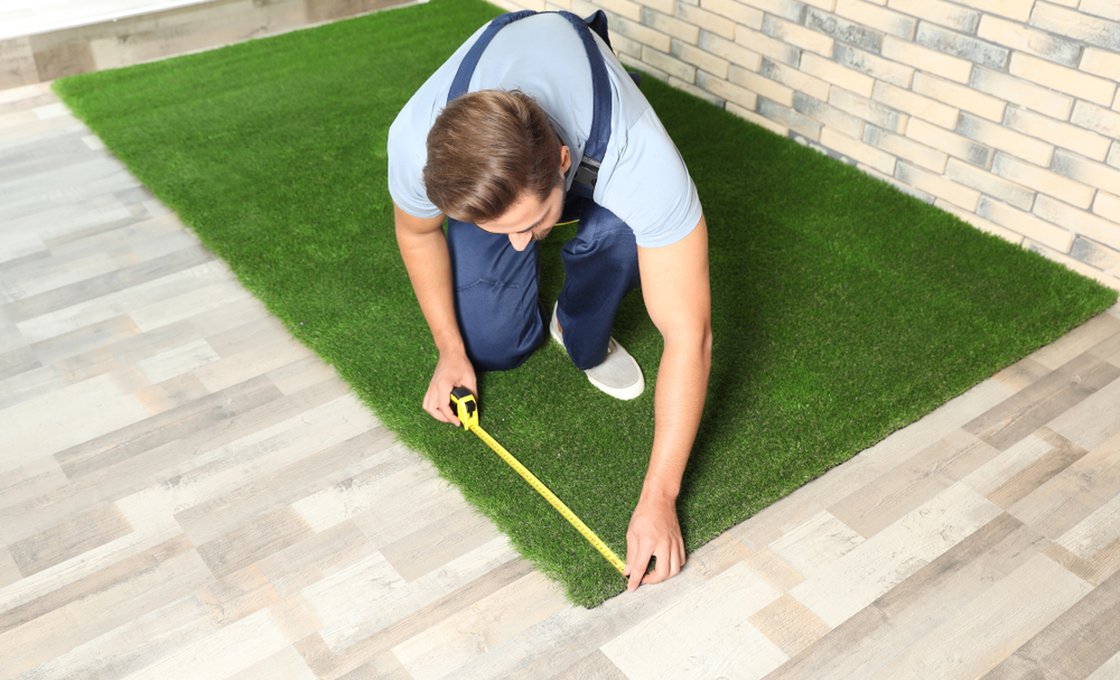 Worker measuring artificial grass mat over an indoor floor