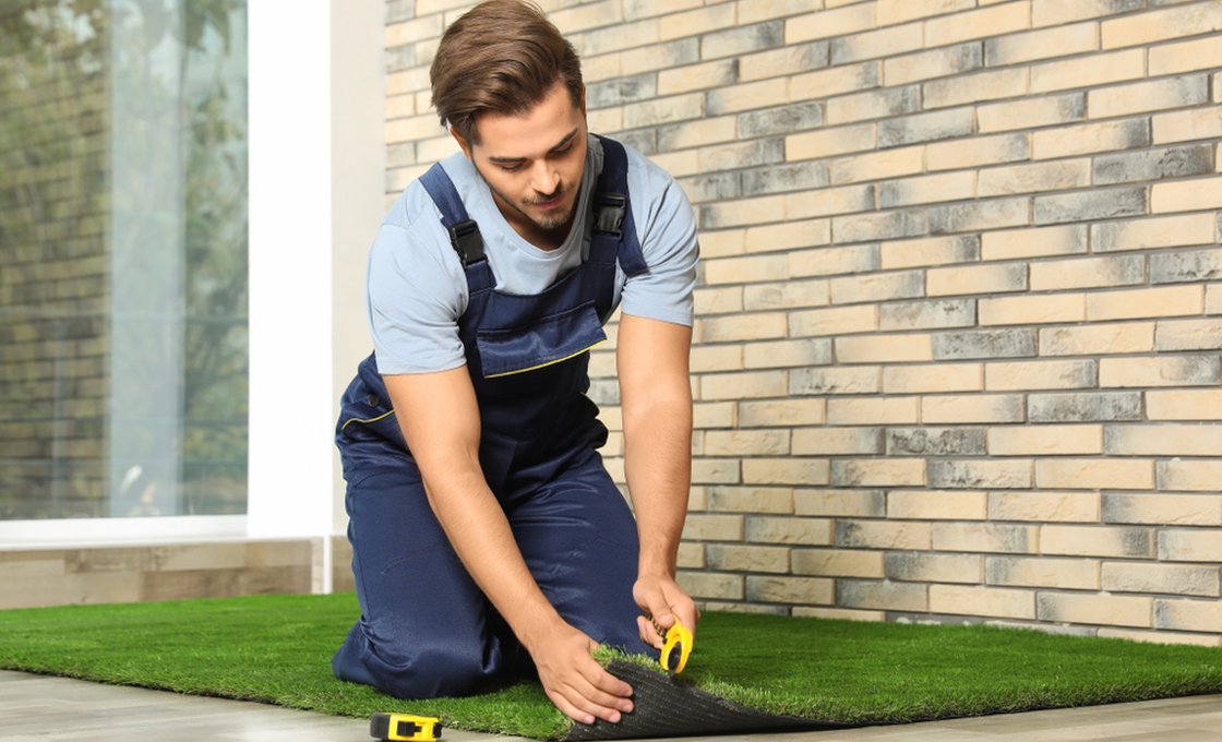 Installation worker trimming artificial grass edges on a commercial lawn