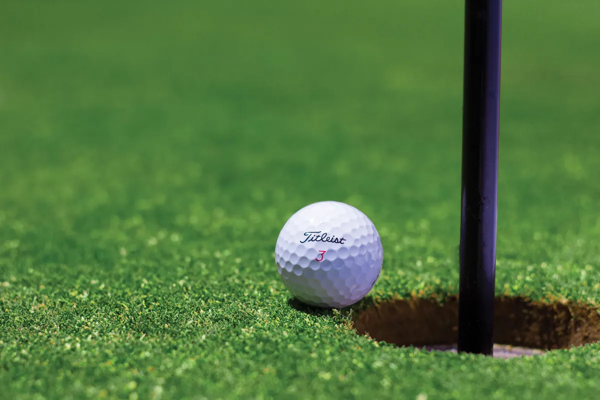 Bola de golfe pousada perto do buraco em um green de putting