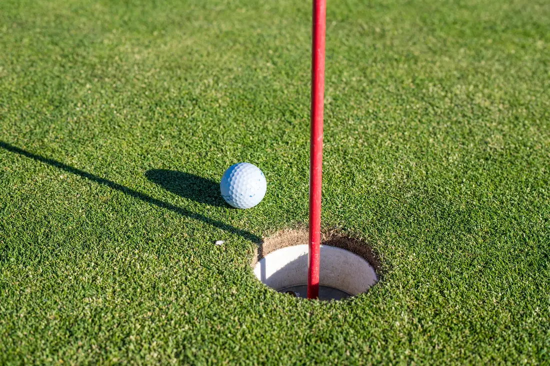 Bola de golfe perto do buraco ao lado de uma bandeira vermelha