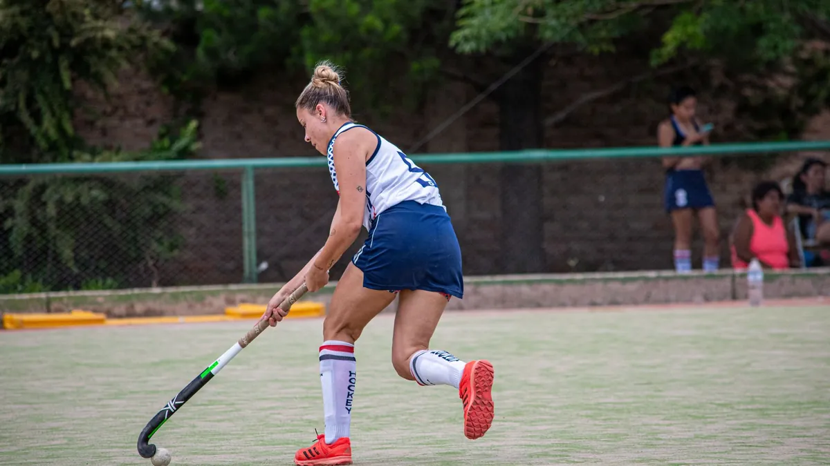 Joueuse de hockey sur gazon sur un terrain vert avec une clôture derrière elle