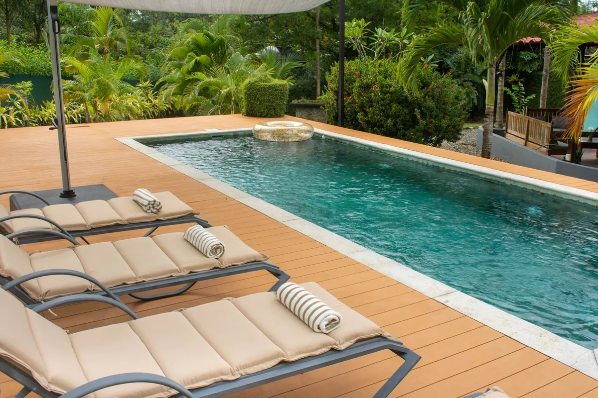 Outdoor pool with deck chairs and lush greenery in sunlight
