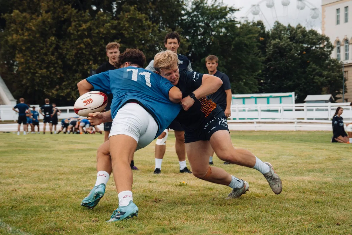 Rugby squad running a contact drill on a training pitch