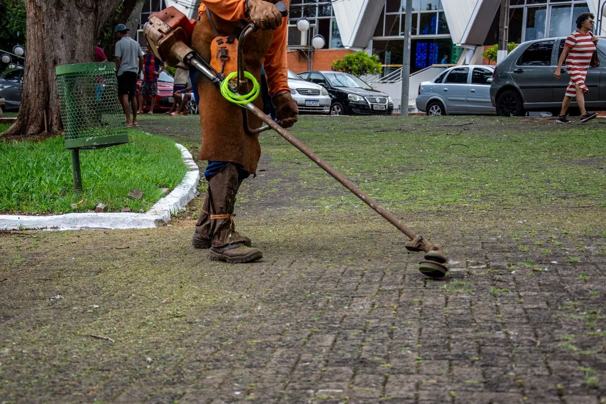 A worker maintaining a green park with a trimmer