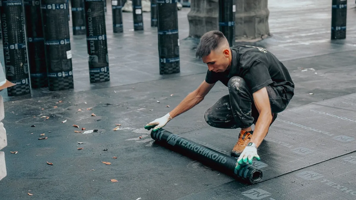 Wide artificial turf roll being unrolled across a compacted crushed-stone stadium sub-base
