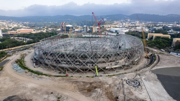 Aerial view of a large stadium under construction, surrounded by cranes.